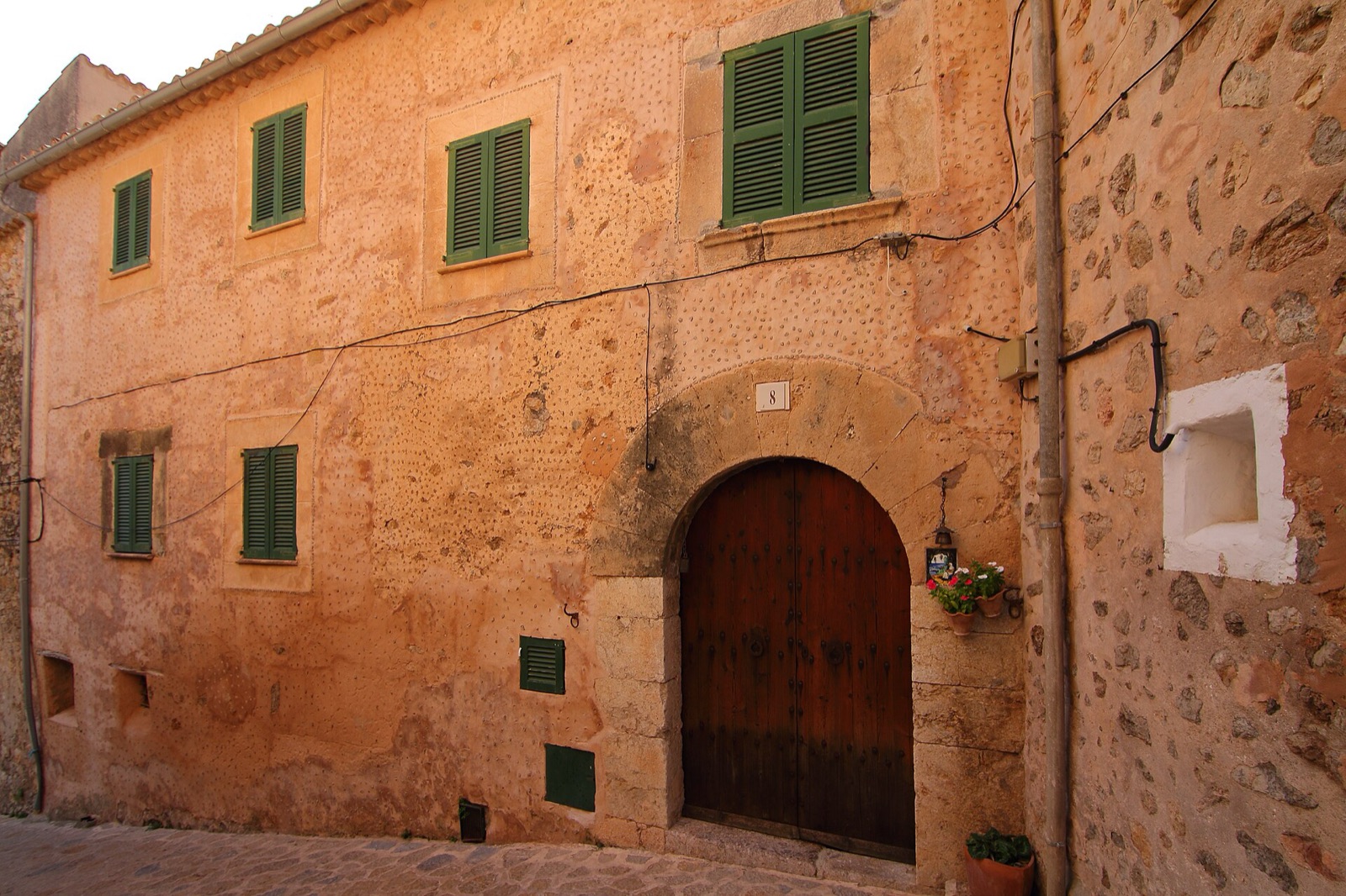 A stone house with green shutters and an arched wooden door in Valldemossa